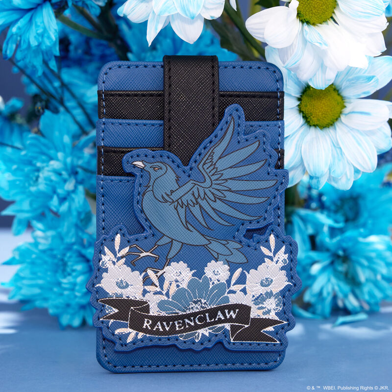Blue and black card holder featuring the Ravenclaw raven as an appliqué in the front, standing on top of blue and white flowers, sitting against a blue background in front of a real bouquet of blue and white flowers 